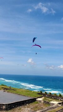 Paragliders Soaring Over Coastal Ocean Waves Under Clear Blue Sky