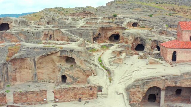 Uplistsikhe cave town fills elevated aerial view with rock halls, winding paths and a historic church near Gori, supporting ancient history, museum tourism and heritage destination promotion.