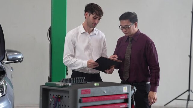Auto repair technician and mechanic lead customer inspection with clipboard in workshop, maintenance discussion and vehicle diagnostic cost estimate beside tool chest in garage, focused teamwork