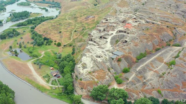 Drone circles above Uplistsikhe cave city in Georgia, revealing rock-cut chambers, the Kura River and surrounding plains for archaeological tourism, cultural heritage media and travel promotion.