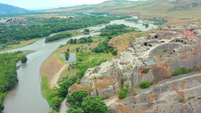 Drone moves sideways across Uplistsikhe in Georgia, presenting carved caves, ancient pathways and the Kura River valley for heritage tourism, archaeology education and destination advertising.