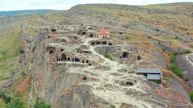 Drone retreats from Uplistsikhe cave city in Georgia, widening across carved chambers, rocky cliffs and open valleys for heritage tourism, historical education and destination promotion campaigns.