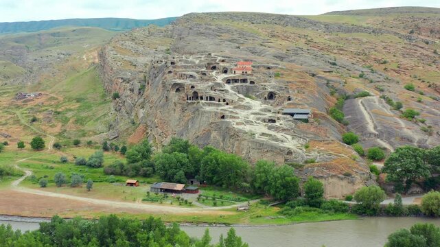 Drone flies backward from Uplistsikhe in Georgia, revealing the full rock-cut settlement, church, riverbank and plains for archaeology documentaries, cultural travel and preservation projects.