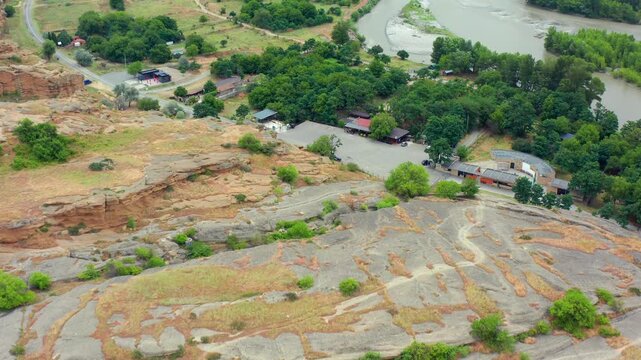 Aerial drone flies forward above Uplistsikhe in Georgia, crossing carved rock terraces, access roads and the Kura River bank for archaeological tourism, heritage media and regional travel promotion.