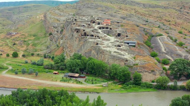 Drone flies forward toward Uplistsikhe in Georgia, approaching the ancient cave city above the Kura River for heritage tourism, archaeology education and cultural destination marketing campaigns.