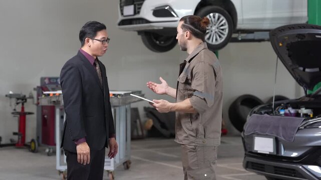 Car mechanic and customer handshake at auto repair service garage, technician with clipboard and tablet explains maintenance checklist and estimate beside vehicle on lift, hood open