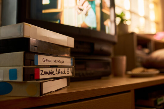 Close up of VHS cassette stack sitting beside television, showing home entertainment, retro media storage, nostalgic viewing habits. Ideal for vintage marketing, streaming comparison content
