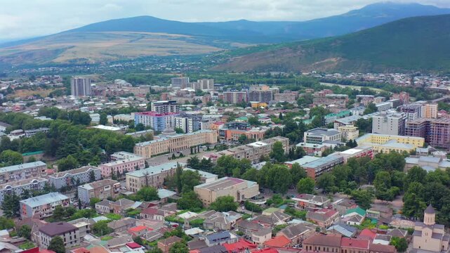 Aerial drone moves sideways across Gori in Georgia, revealing the fortress district, residential blocks and mountain backdrop for urban tourism, city geography, development and destination media.