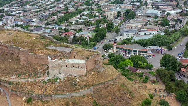 Gori Fortress fills circling aerial view above stone walls, rocky slopes and surrounding neighborhoods, supporting heritage tourism, archaeology, city history and Georgian landmark media campaigns.