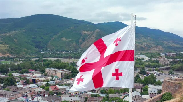 Georgian flag waves in aerial view above Gori and forested hills, supporting national identity, patriotic media, country branding, cultural tourism and regional destination promotion in Georgia.