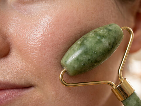 Woman using green jade roller massager on cheek for facial skin care
