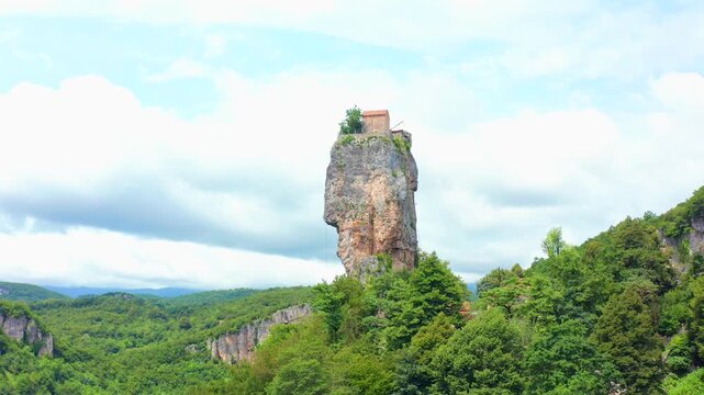 Drone takes off near Katskhi Pillar in Georgia, rising toward the limestone monolith and summit church above dense forest for religious tourism, pilgrimage, geology and cultural heritage projects.