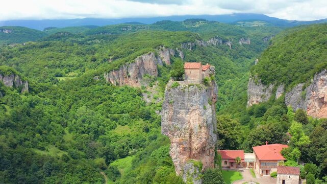 Drone flies forward toward Katskhi Pillar in Georgia, approaching the isolated limestone monolith and summit church above a forested valley for pilgrimage, heritage tourism and travel promotion.