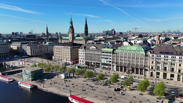 Hamburg, Hamburg, Germany - 29 April 2026: Aerial view of Jungfernstieg featuring historic buildings, green trees, and the Alster lake waterfront under a clear blue sky.