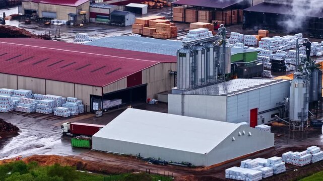 Aerial view of a lumber processing facility with stacks of timber, industrial buildings, and silos in Latvia.