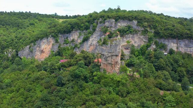 Katskhi Pillar stands in aerial view across dense forest and layered limestone cliffs near Chiatura, supporting geotourism, pilgrimage travel, regional mapping and Georgian destination media.