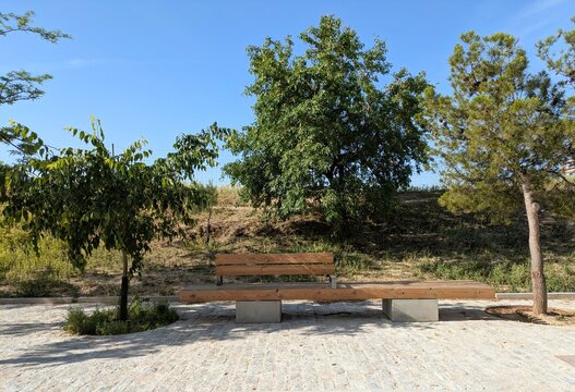 Moderno banco de madera con respaldo, apoyado sobre dos bloques de hormig&oacute;n, en un pavimento de losas de piedra de un parque p&uacute;blico