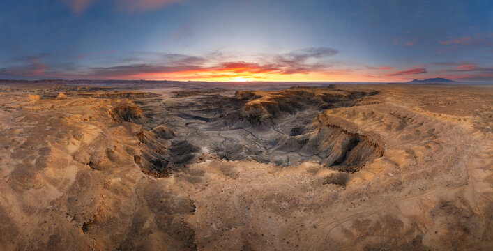 Aerial view of the rugged badlands landscape with deep canyons and eroded rock formations under a dramatic sunset sky in Hanksville, Utah, United States.