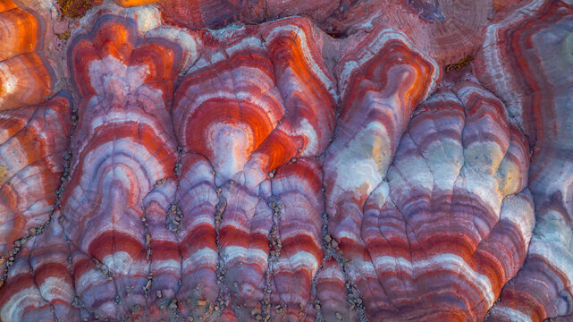 Aerial view of colorful striped badlands in Hanksville, featuring vibrant red, orange, and white sedimentary rock layers eroded into intricate patterns. Hanksville, Utah, United States.