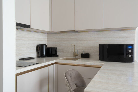 Clean modern kitchen with light grey cabinets, sleek countertops, a built in sink, microwave, electric kettle, and induction hob, creating a functional and stylish home interior