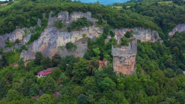Aerial drone orbits Katskhi Pillar in Georgia, revealing the vertical limestone formation, hilltop chapel and forest valley for heritage travel, pilgrimage campaigns and nature documentary use.