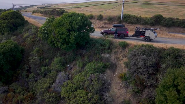 Aerial views show a teardrop camper trailer parked on the side of the road in California. Adventure and free camping are here.