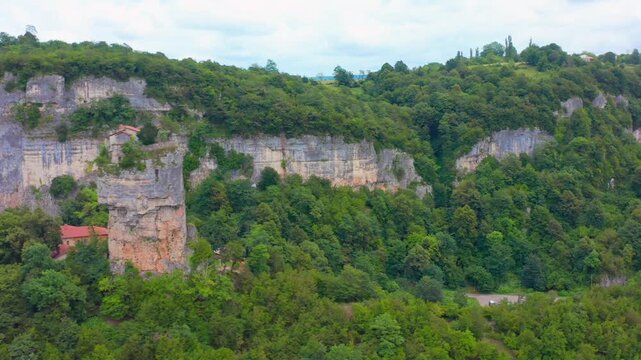 Aerial drone tracks sideways across Katskhi Pillar in Georgia, showing the remote monastery above a sheer rock column for cultural tourism, spiritual travel, geology and landmark advertising.