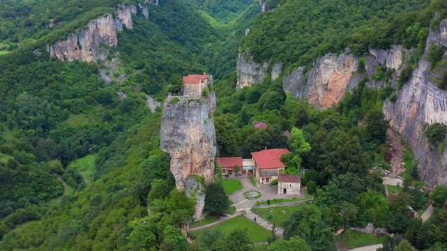 Aerial drone rises above Katskhi Pillar in Georgia, expanding from the monastery grounds to the limestone column and forest valley for religious tourism, archaeology and destination campaigns.