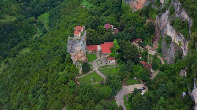 Aerial drone descends toward Katskhi Pillar in Georgia, lowering above the summit church, monastery complex and wooded gorge for pilgrimage travel, heritage promotion and cultural education.