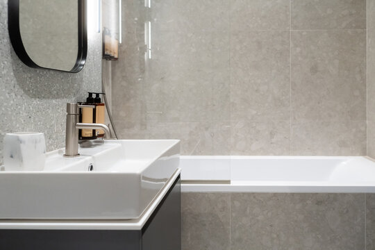 Modern bathroom interior featuring a contemporary white sink, sleek faucet, frameless mirror, and a clean bathtub, showcasing hygiene, comfort, and stylish utility in home living