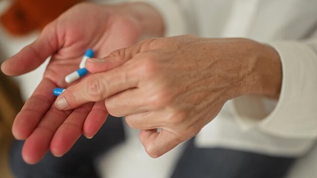 Woman holding blue and white pills in open hands, finger picking a capsule in a building interior while seated and counting medication; concern.
