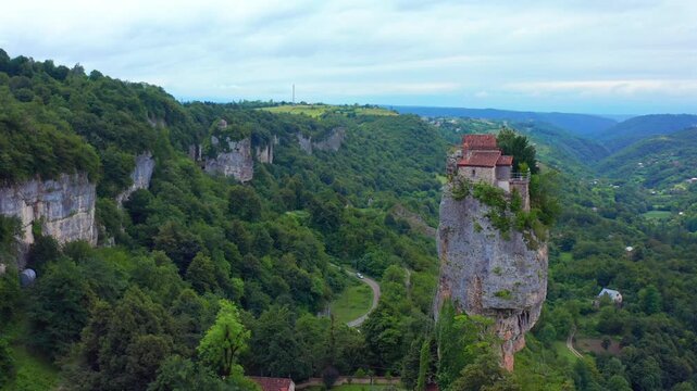 Katskhi Pillar approaches through aerial view above a winding valley road and forested cliffs near Chiatura, supporting landmark tourism, pilgrimage routes, regional geography and travel campaigns.