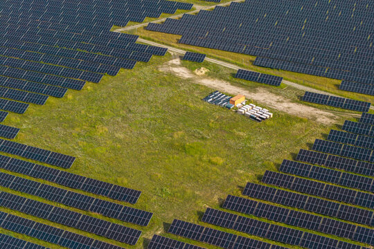 Aerial view of a vast solar farm with rows of photovoltaic panels installed in a green field, featuring a small cluster of equipment containers in the center, Poland.