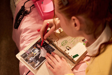 Teenager girl arranging photo album and writing notes in scrapbook, documenting memories and...