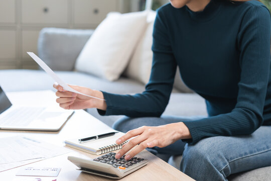 Stressed asian young business woman, employee using calculator to calculate expenses of monthly, hand holding bills and receipt for to payment on table at home. Financial, finance of banking concept.