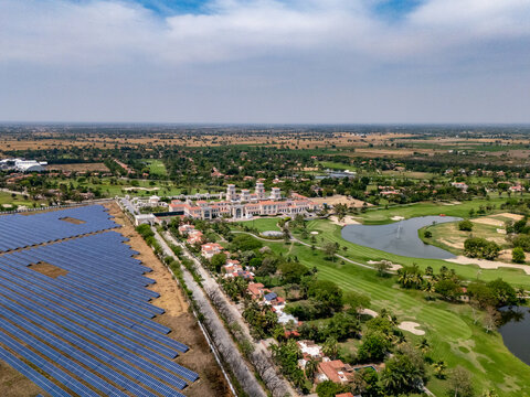 Ahmedabad, Gujarat, India - 21 March 2026: Aerial view of Kalhaar Blues Greens Golf Club with lush fairways, a pond, and an adjacent solar panel farm under a clear sky.