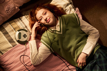 Portrait of Caucasian teenage girl listening through headphones beside portable CD player while...