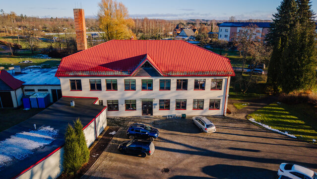 Burtnieki, Latvia - 22 November 2025: Aerial view of a rural school building with a distinctive red roof, surrounded by trees and a parking area on a sunny late autumn day.