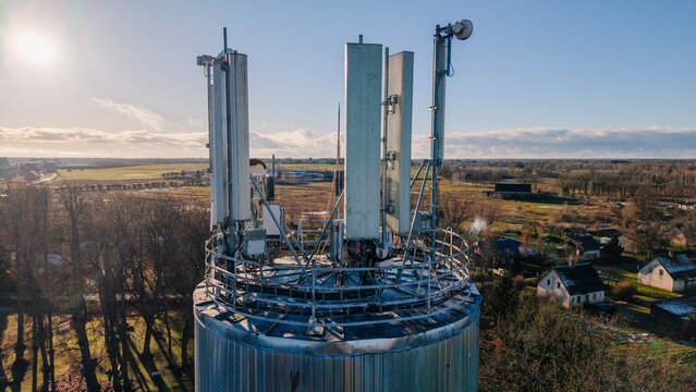 Valmiera, Latvia - 11 November 2025: Aerial view of a telecommunications tower with antennas and satellite dishes set against a rural landscape under a clear sky.