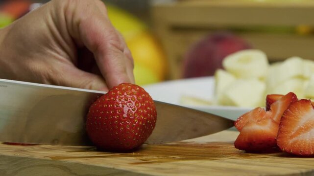 Knife slicing through delicious, juicy strawberry on cutting board - closeup shot