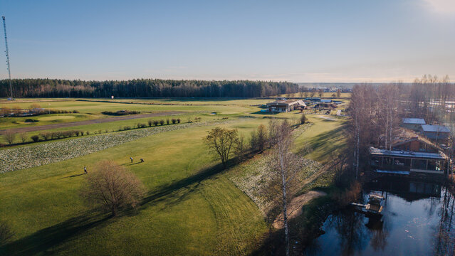 Valmiera, Latvija - 18 November 2025: Aerial view of a golf club building and course on a frosty morning with golfers on the green, a small pond, and surrounding trees.