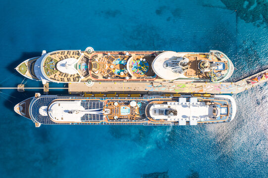 The Bahamas - 15 December 2022: Aerial view of two large cruise ships docked at the pier at CocoCay, featuring turquoise waters, swimming pools, and water slides on the decks.