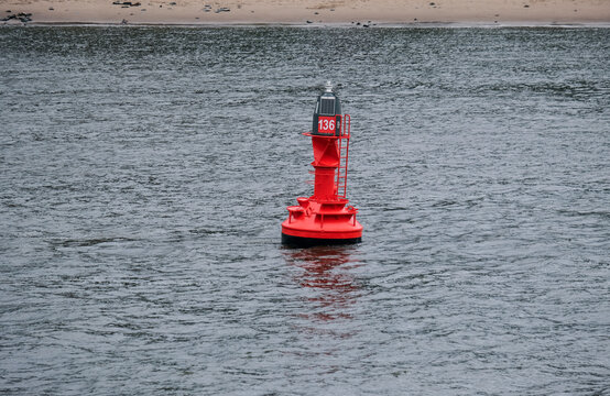 Sicherheit und Navigation im Fluss Elbe: Eine der roten Bojen in der Elbe von Hamburg bis ins Meer zur Fahrwassermarkierung f&uuml;r gro&szlig;e und kleine Schiffe mit einem Teil Elbestrand im Hintergrund
