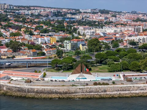 Lisboa, Portugal - 25 July 2026: Aerial view of the Monument to the Overseas Combatants along the waterfront, surrounded by green parks, urban buildings, and the Lisbon cityscape.