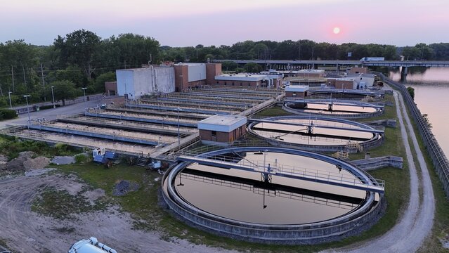 Monroe, Michigan, United States - 25 July 2026: Aerial view of the Monroe Water Department with circular sedimentation tanks and rectangular basins along the river at sunset.