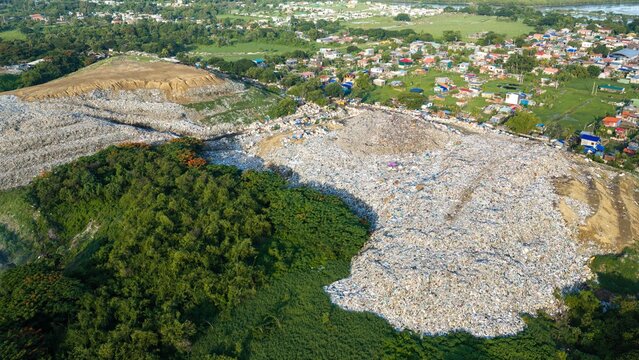 Iloilo City, Philippines - 25 July 2026: Aerial view of the Iloilo City Landfill, showing large piles of waste surrounded by lush vegetation and nearby residential areas.
