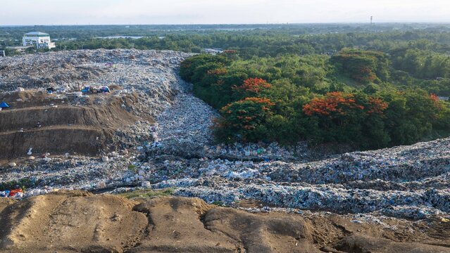Iloilo City, Philippines - 25 July 2026: Aerial view of the Iloilo City Landfill showing a large expanse of waste adjacent to dense green trees and flowering plants.