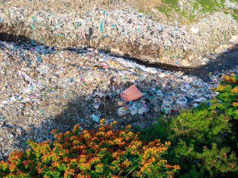 Iloilo City, Philippines - 25 July 2026: Aerial view of the Iloilo City Landfill with piles of waste, a small orange tent, and people sorting through garbage near lush green trees.