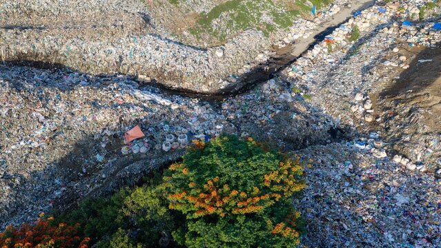 Iloilo City, Western Visayas, Philippines - 25 July 2026: Aerial view of Iloilo City Landfill, showing vast piles of waste, plastic debris, and a drainage channel with scattered trees.