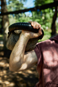 Vertical shot of Caucasian young adult man lifting kettlebell at outdoor gym, training strength and endurance. Ideal for fitness marketing, workout programs, healthy lifestyle content